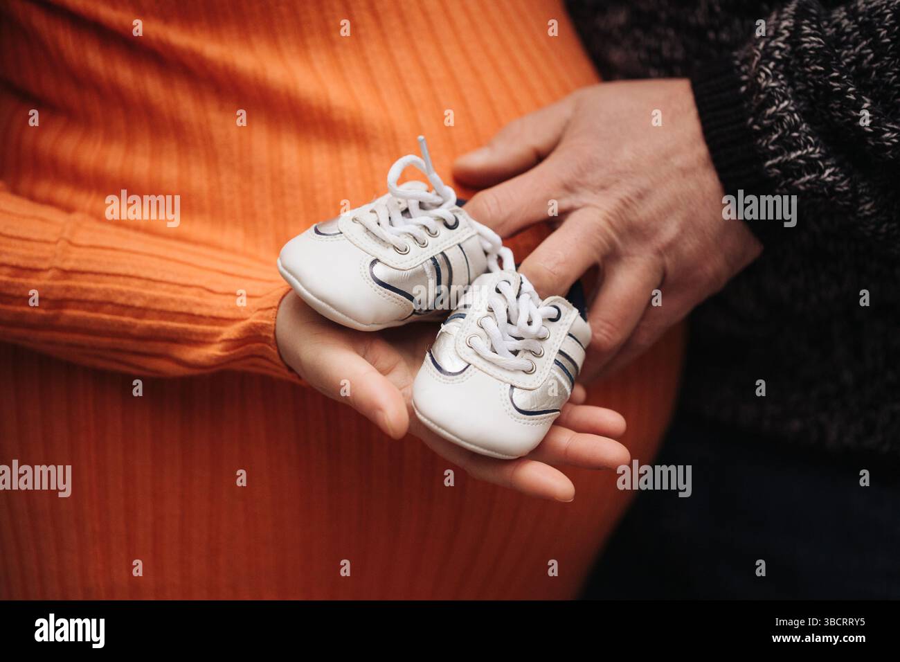 Photo de famille de grossesse. L'homme et la femme tiennent des chaussures de bébé. Amour et soins parentaux. En attendant le nouveau-né ensemble. Mains sur le ventre. En attendant une nouvelle vie. Banque D'Images
