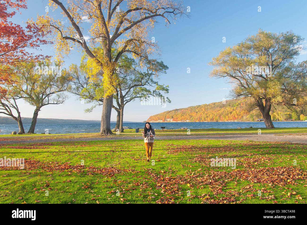 Une femme chinoise marchant à travers Clute Park sur le lac Seneca en fin d'après-midi coucher de soleil en automne dans le nord de l'État de New york. Banque D'Images