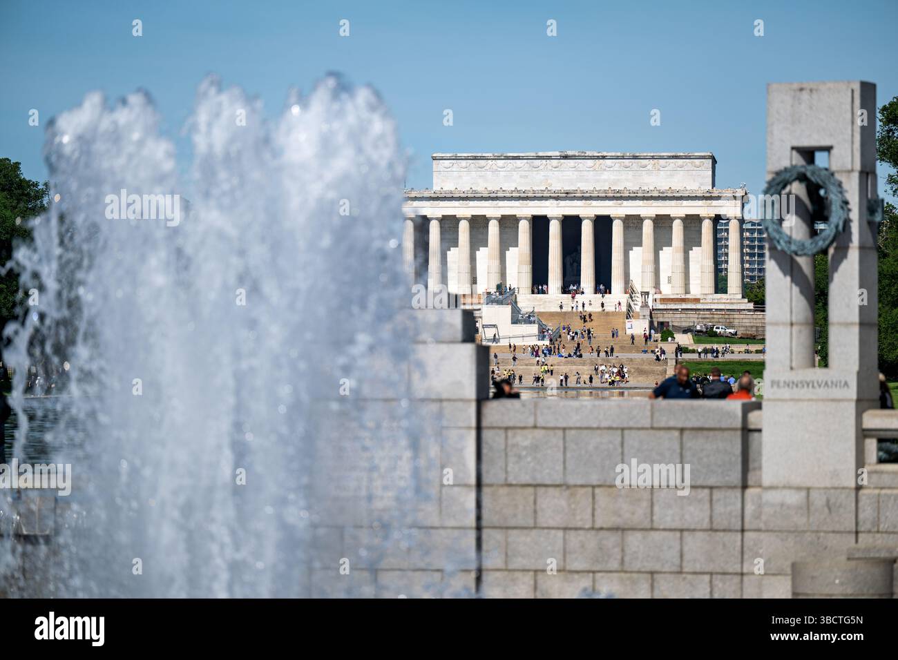 Fontaine du Mémorial de la Seconde Guerre mondiale avec le Mémorial de Lincoln au loin Washington DC | WASHINGTON DC — La fontaine du Mémorial de la Seconde Guerre mondiale se dresse de manière proéminente sur le National Mall, avec l’emblématique Mémorial de Lincoln visible au loin. Achevé en 2004, le Mémorial de la Seconde Guerre mondiale rend hommage aux 16 millions d’Américains qui ont servi dans les forces armées pendant la guerre, dont plus de 400 000 ont perdu la vie. Le mémorial comprend une piscine centrale du Rainbow entourée de 56 piliers en granit représentant les États et territoires des États-Unis pendant la guerre. Situé à l’extrémité est de la piscine réfléchissante, le mémo Banque D'Images