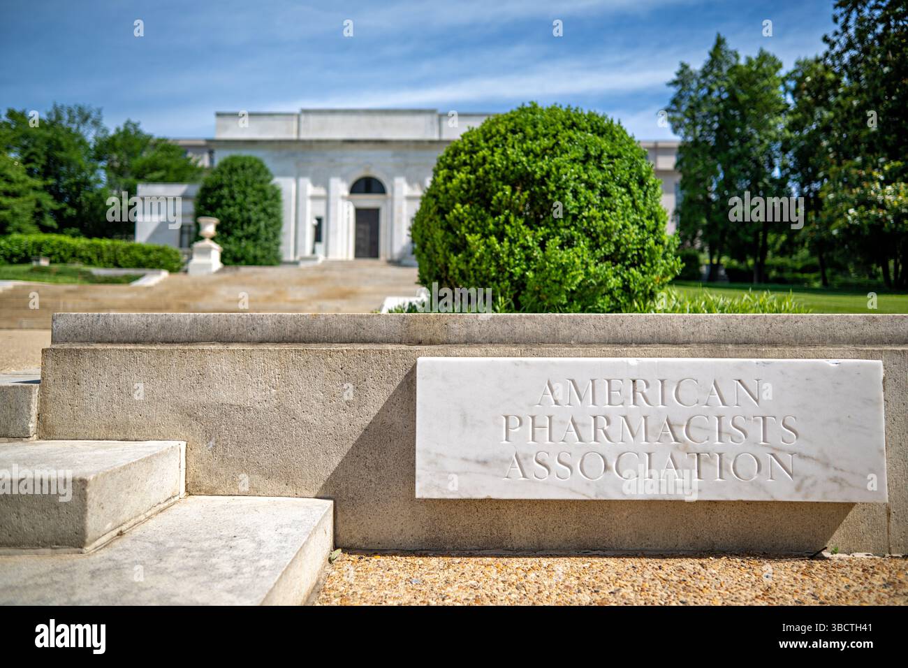 WASHINGTON DC — Une enseigne de marbre pour l'American Pharmacists Association est exposée devant le siège de l'organisation sur Constitution Avenue, en face du Lincoln Memorial. Conçu par le célèbre architecte John Russell Pope et achevé en 1934, ce bâtiment néoclassique abrite la première société professionnelle de pharmaciens du pays, fondée en 1852. L'impressionnante structure présente une façade monumentale de temple avec six colonnes doriques soutenant un fronton orné de reliefs sculpturaux qui illustrent l'histoire de la pharmacie. Ce monument en marbre blanc et calcaire Banque D'Images