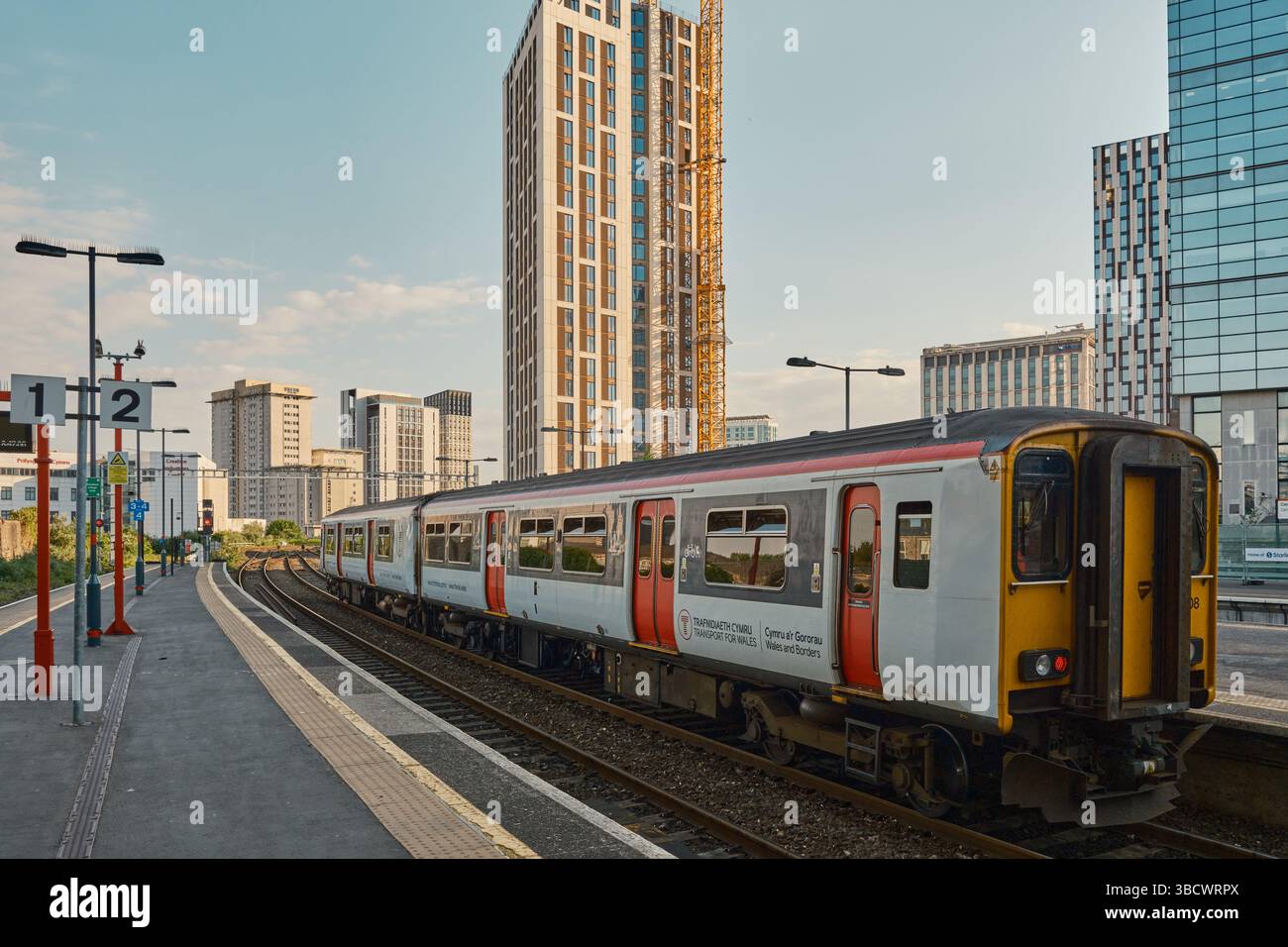 Transport pour le pays de Galles train à la plate-forme de Cardiff Queen Street Station avec des gratte-ciel modernes en arrière-plan, capturés dans la lumière du soir. Banque D'Images