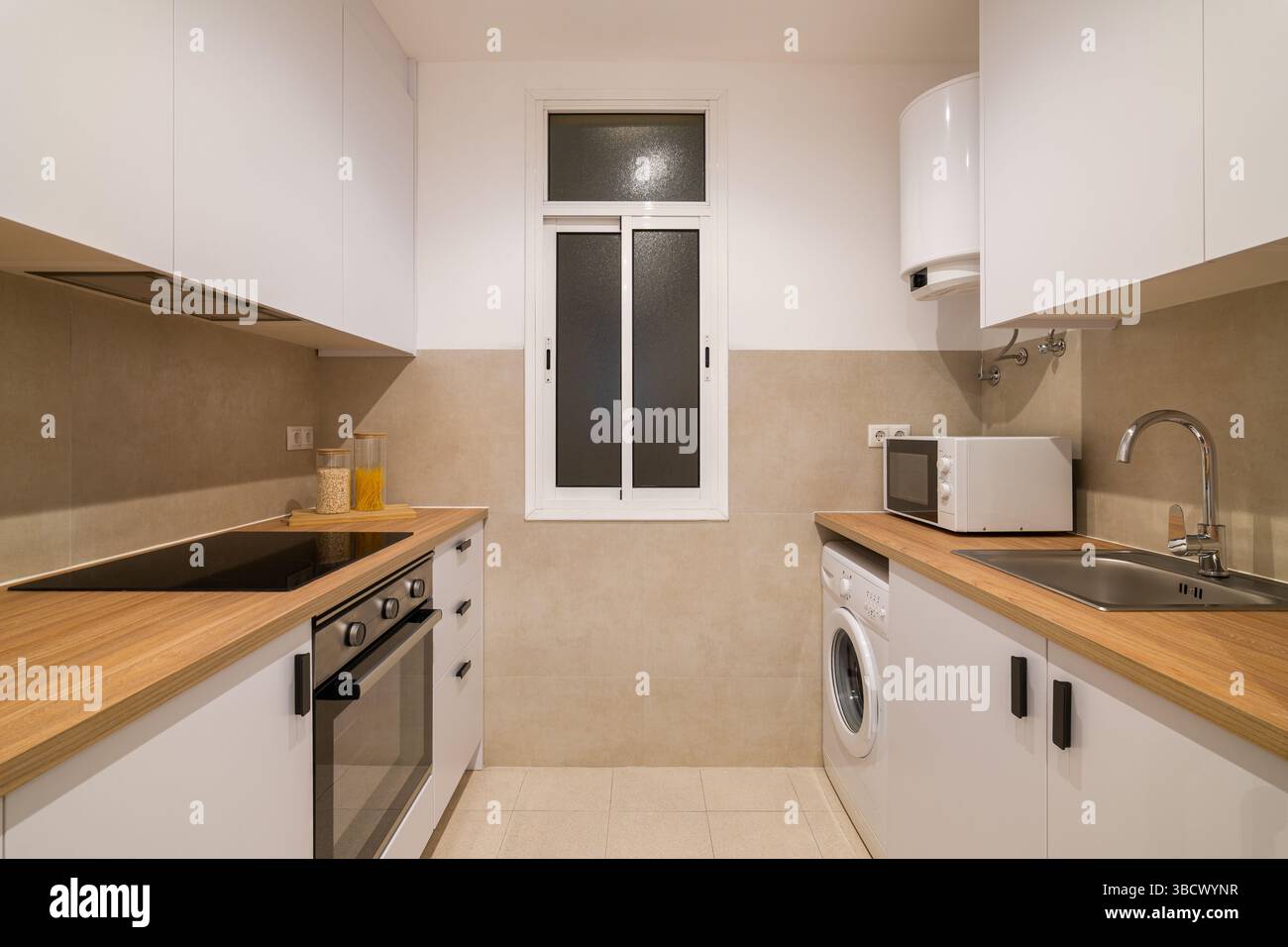 Vue centrale de la cuisine avec armoires blanches, comptoirs en bois, grand réfrigérateur et micro-ondes Banque D'Images