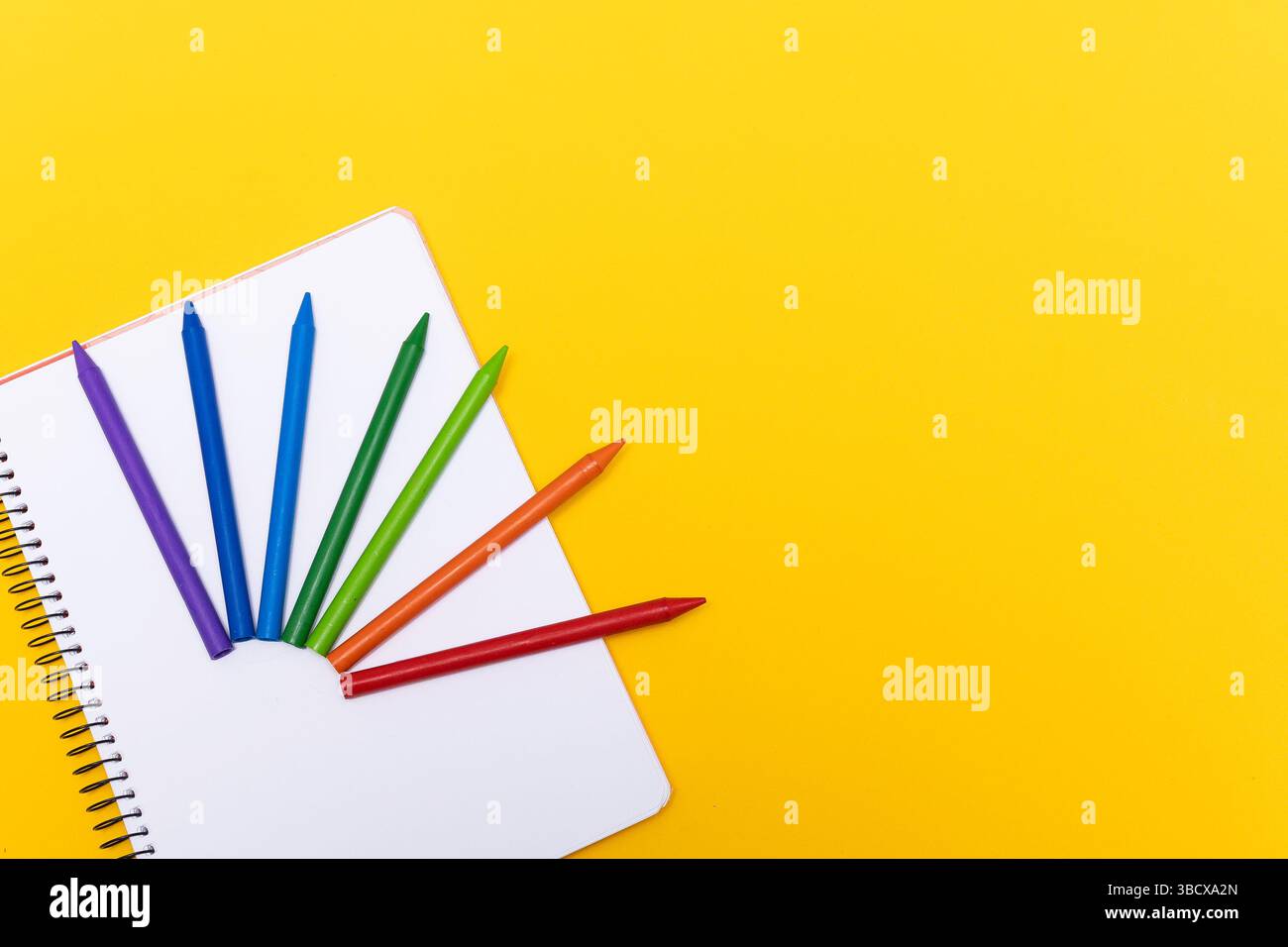 Crayons de couleur disposés en éventail sur un cahier en spirale blanc, placé sur un fond jaune vif. L'image représente l'école, la créativité, l'art. Banque D'Images