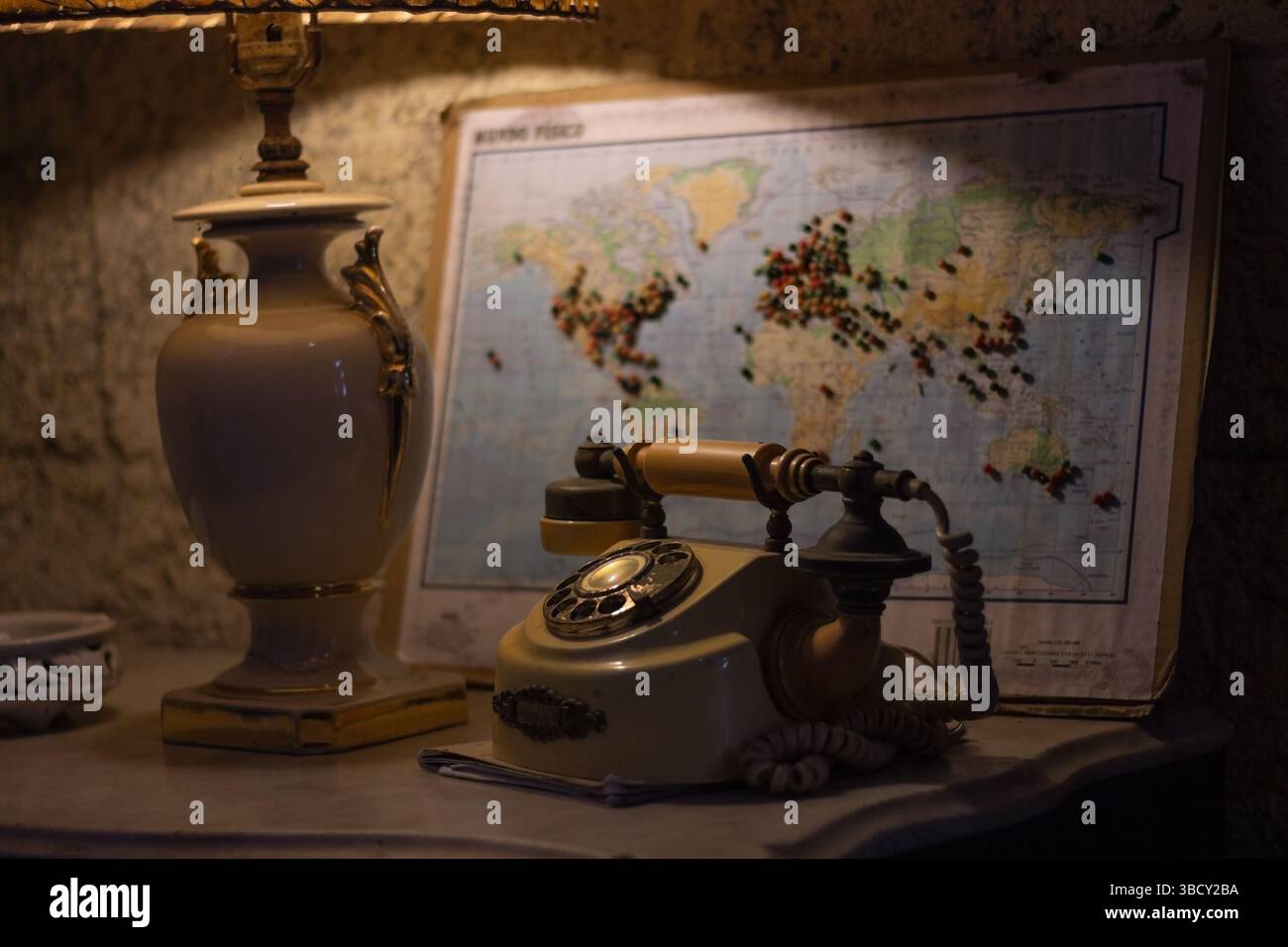 Lampe de chevet diffusant une lueur chaude dans une pièce faiblement éclairée la nuit, avec un téléphone vintage et une carte du monde en arrière-plan Banque D'Images