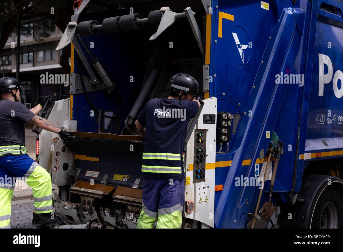 Porto, Portugal - 05.04.2025 : camion à ordures bleu avec des ouvriers suspendus à l'arrière. Service de nettoyage urbain. Banque D'Images