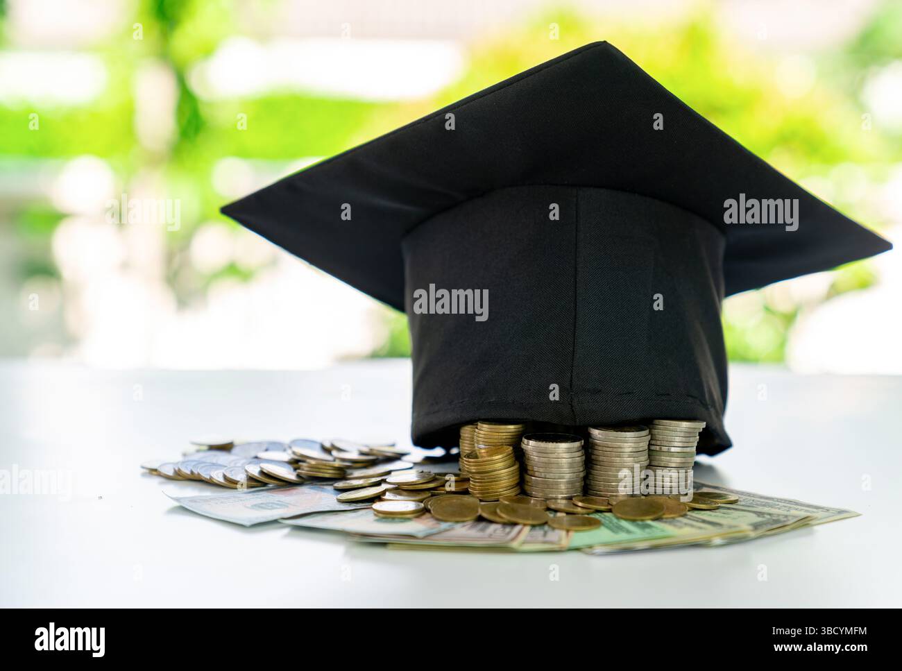 Une casquette de graduation placée sur une pile de pièces de monnaie et de billets d'un dollar, avec un fond flou. Banque D'Images