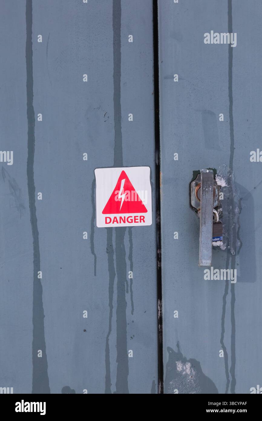 Pictogramme d'avertissement de danger rouge sur blanc sur la porte de l'armoire électrique verrouillée en métal gris avec glace fondante en hiver, Québec, Canada Banque D'Images