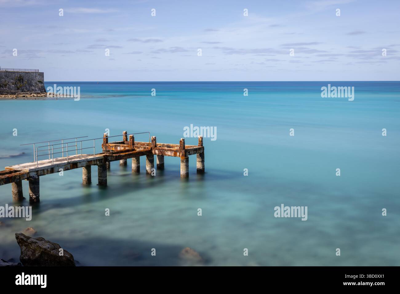 Jetée rouillée au-dessus des eaux turquoises des Bermudes, capturée avec une longue exposition pour créer un paysage marin lisse et des tons pastel sous un ciel clair. Banque D'Images Jetée rouillée au-dessus des eaux turquoises des Bermudes, capturée avec une longue exposition pour créer un paysage marin lisse et des tons pastel sous un ciel clair. Banque D'Images