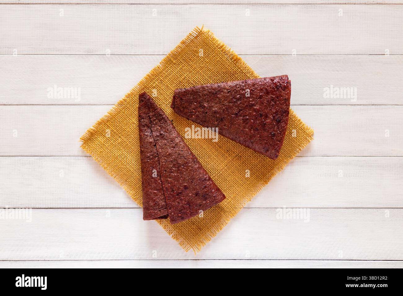 Deux morceaux de pastille de fruits triangulaires rouges affichés sur tissu jaune sur fond de bois blanc à partir de l'angle supérieur Banque D'Images
