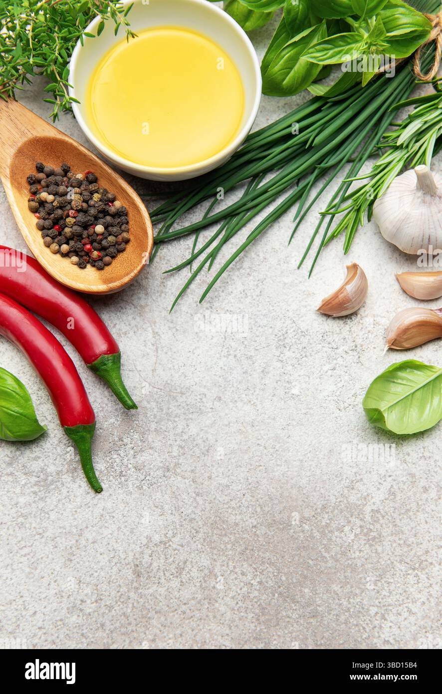 Herbes culinaires fraîches, épices, ail, piments et huile d'olive sont disposés sur un fond gris, offrant un affichage vibrant pour la nourriture et la cuisine c Banque D'Images