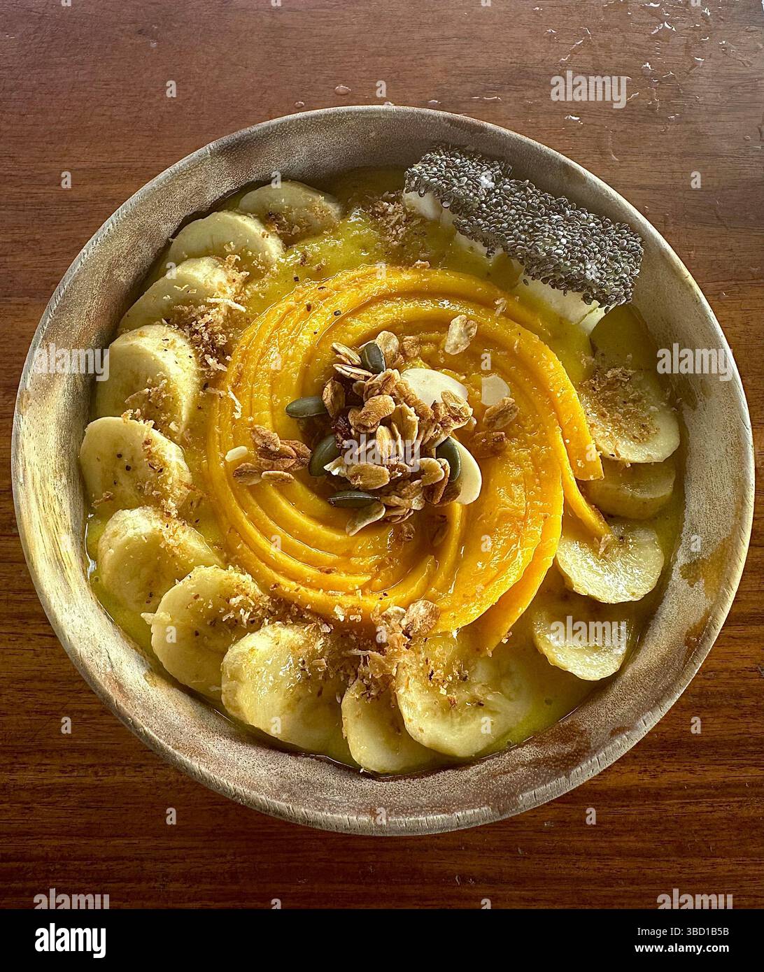 Bol à smoothie vibrant avec banane, mangue, granola, graines et flocons de noix de coco, parfait pour une alimentation saine, le bien-être et les thèmes de style de vie alimentaire - Image de stock capturée avec un smartphone
