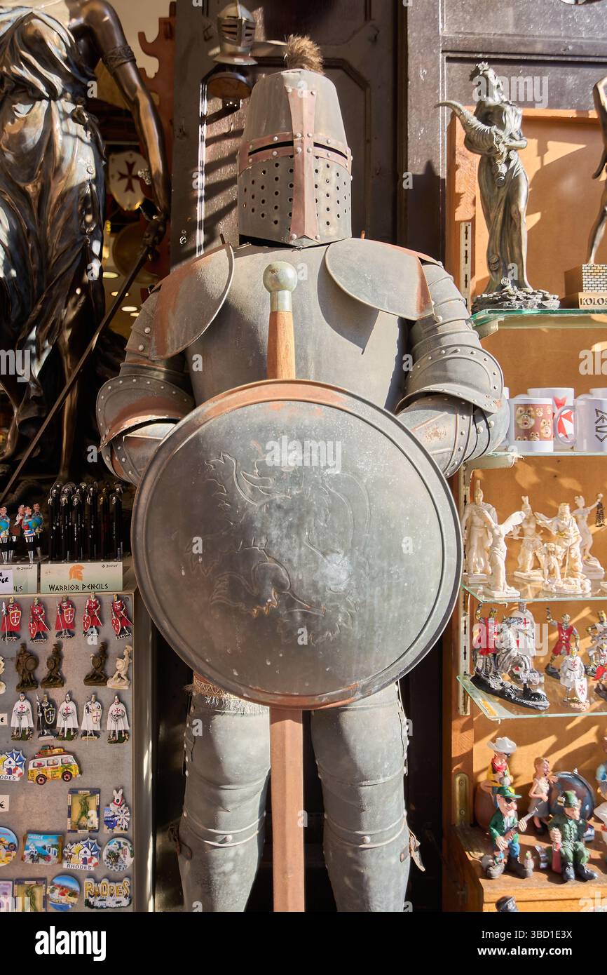 Rodas.Greece - 22 mai 2025 : un costume complet d'armure de chevalier médiéval, complet avec bouclier et épée, se tient bien en évidence à l'extérieur d'une boutique de souvenirs, reflet Banque D'Images