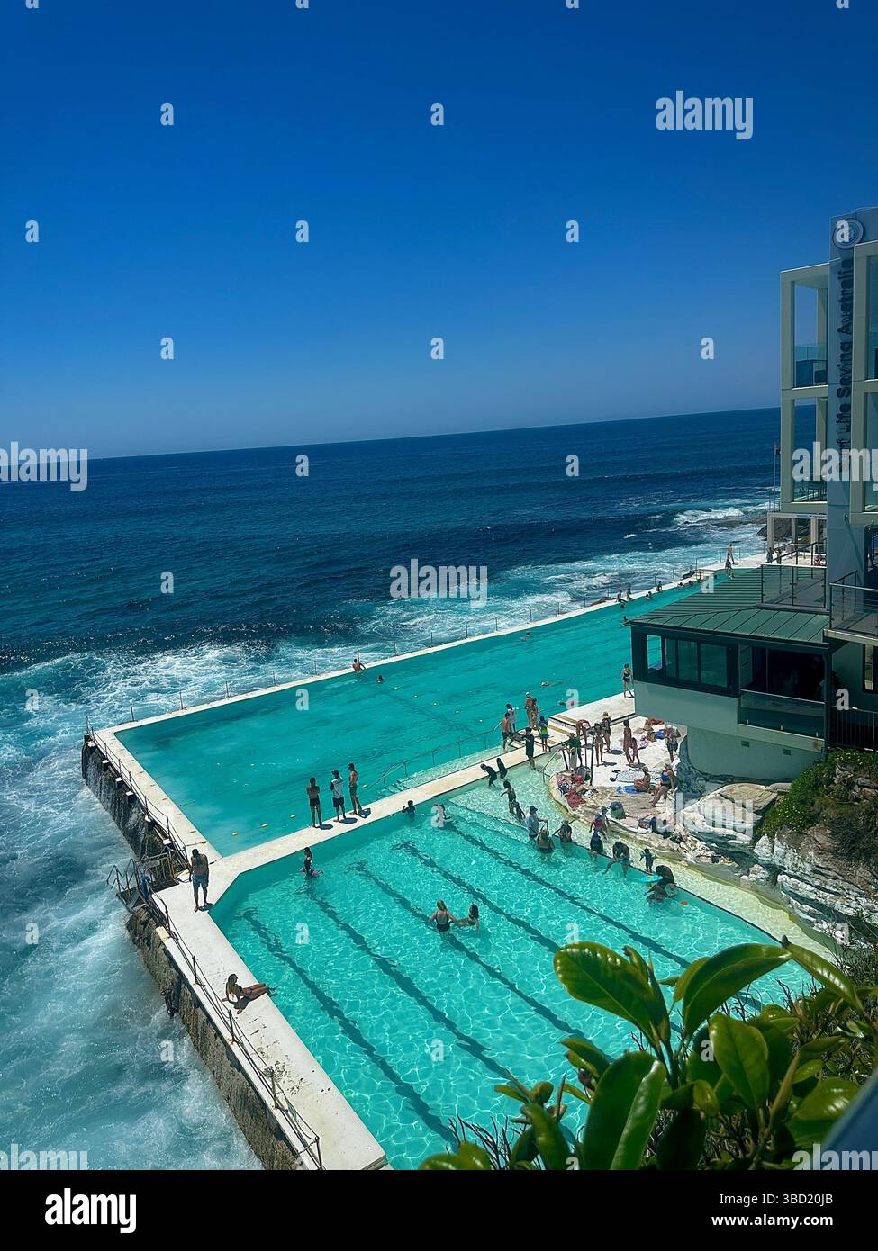 Les touristes profitent d'une journée ensoleillée à la piscine océanique Bondi icebergs avec des vagues s'écrasant contre le bord, emblématique monument côtier de Sydney en été. - Image de stock capturée avec un smartphone