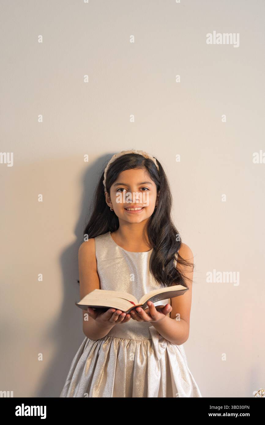 Une jeune fille tient un livre et sourit. Concept d'innocence et de curiosité, car la jeune fille semble profiter de son temps de lecture. Le livre lui-même c Banque D'Images Une jeune fille tient un livre et sourit. Concept d'innocence et de curiosité, car la jeune fille semble profiter de son temps de lecture. Le livre lui-même c Banque D'Images