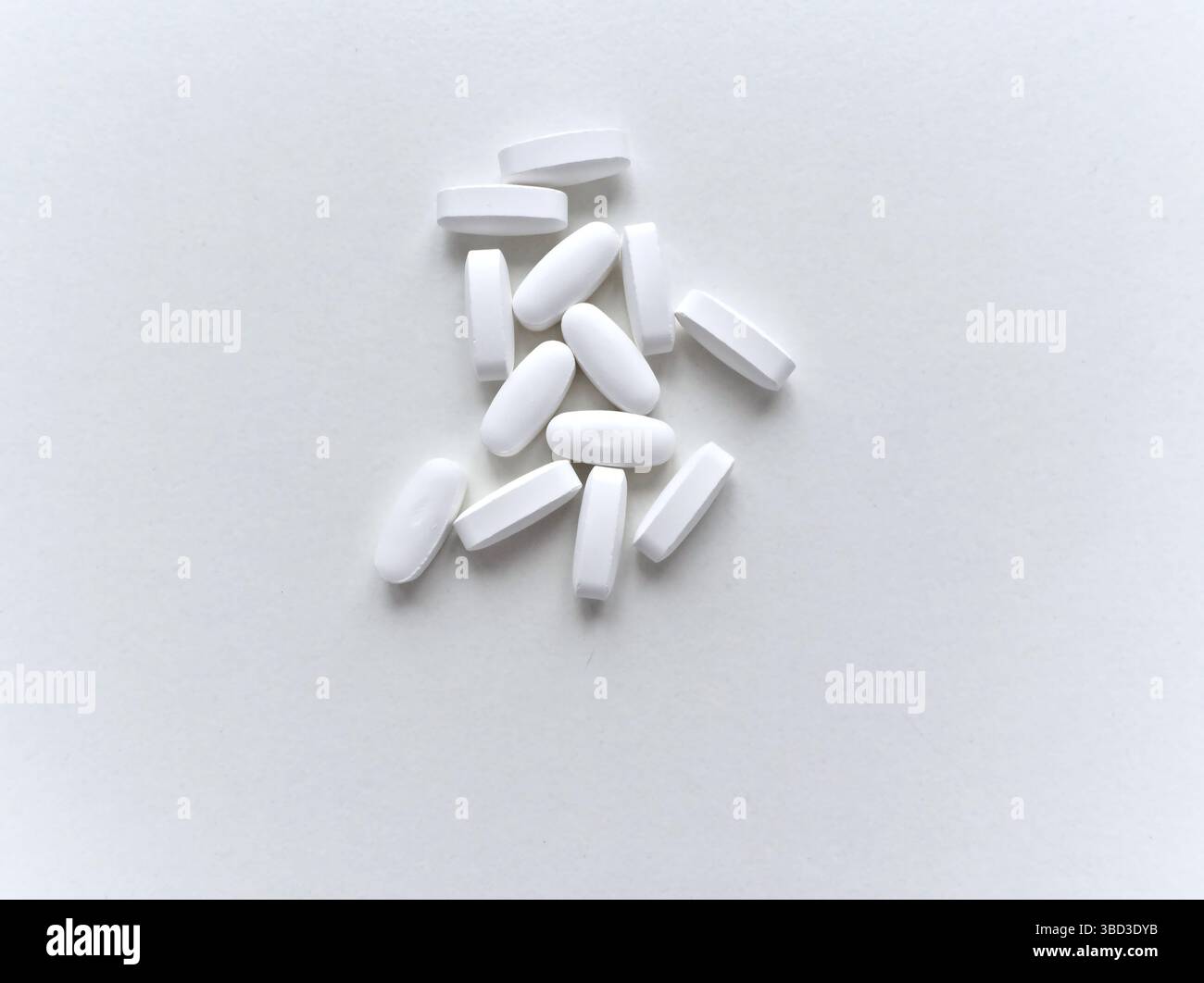 Une pile de pilules blanches sur un fond blanc. Les pilules sont petites et blanches, et elles sont dispersées à travers la surface. Concept d'organisation et ord Banque D'Images