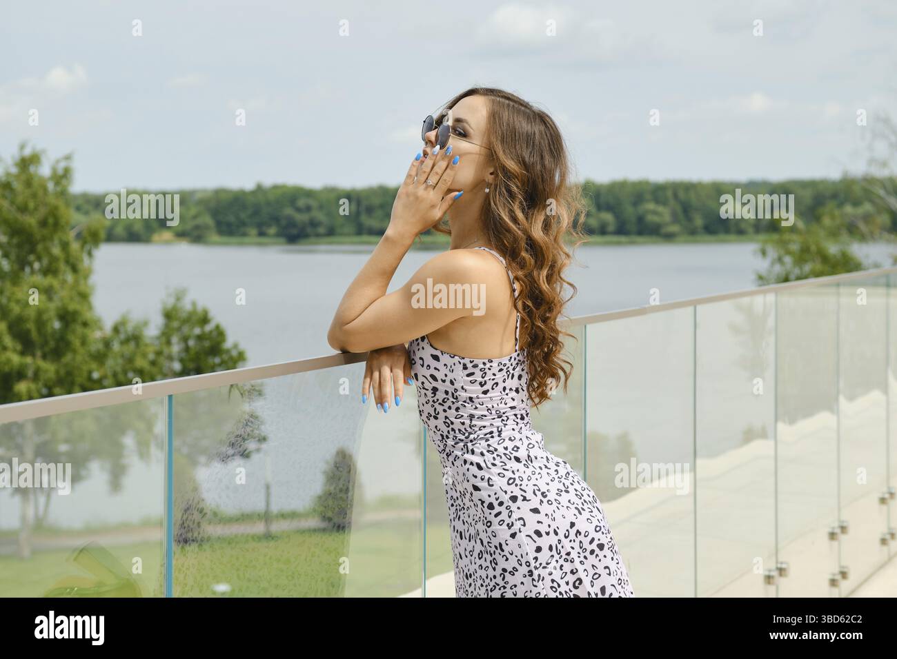 Jeune femme avec de longs cheveux bouclés admirant une belle vue depuis le balcon Banque D'Images
