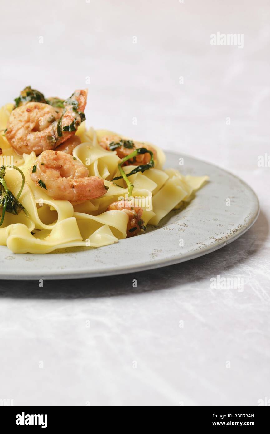 Une portion de fettuccine de crevettes garnie d'herbes fraîches est élégamment présentée sur une assiette grise, mettant en valeur un délicieux mélange de saveurs et de couleurs Banque D'Images