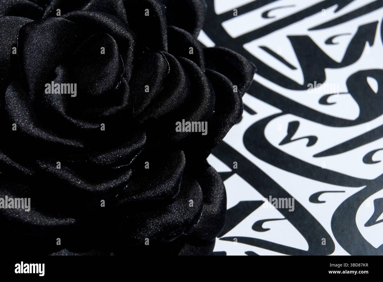 Rose noire placée artistiquement sur fond d'écriture arabe foncé. Banque D'Images