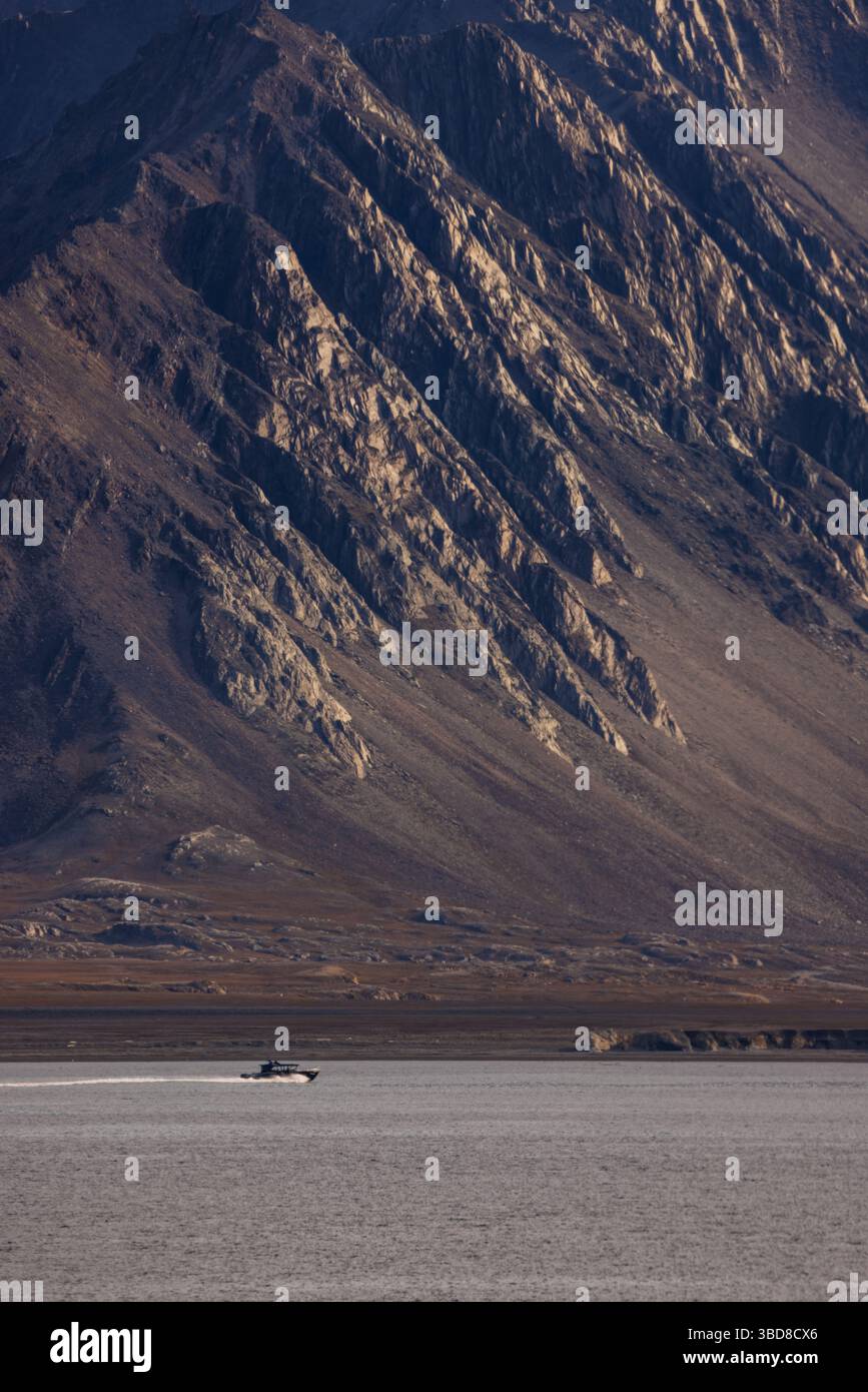 Un bateau à moteur rapide traverse un fjord arctique calme sous les montagnes escarpées du Svalbard, en Norvège, sous la douce lumière estivale. Banque D'Images