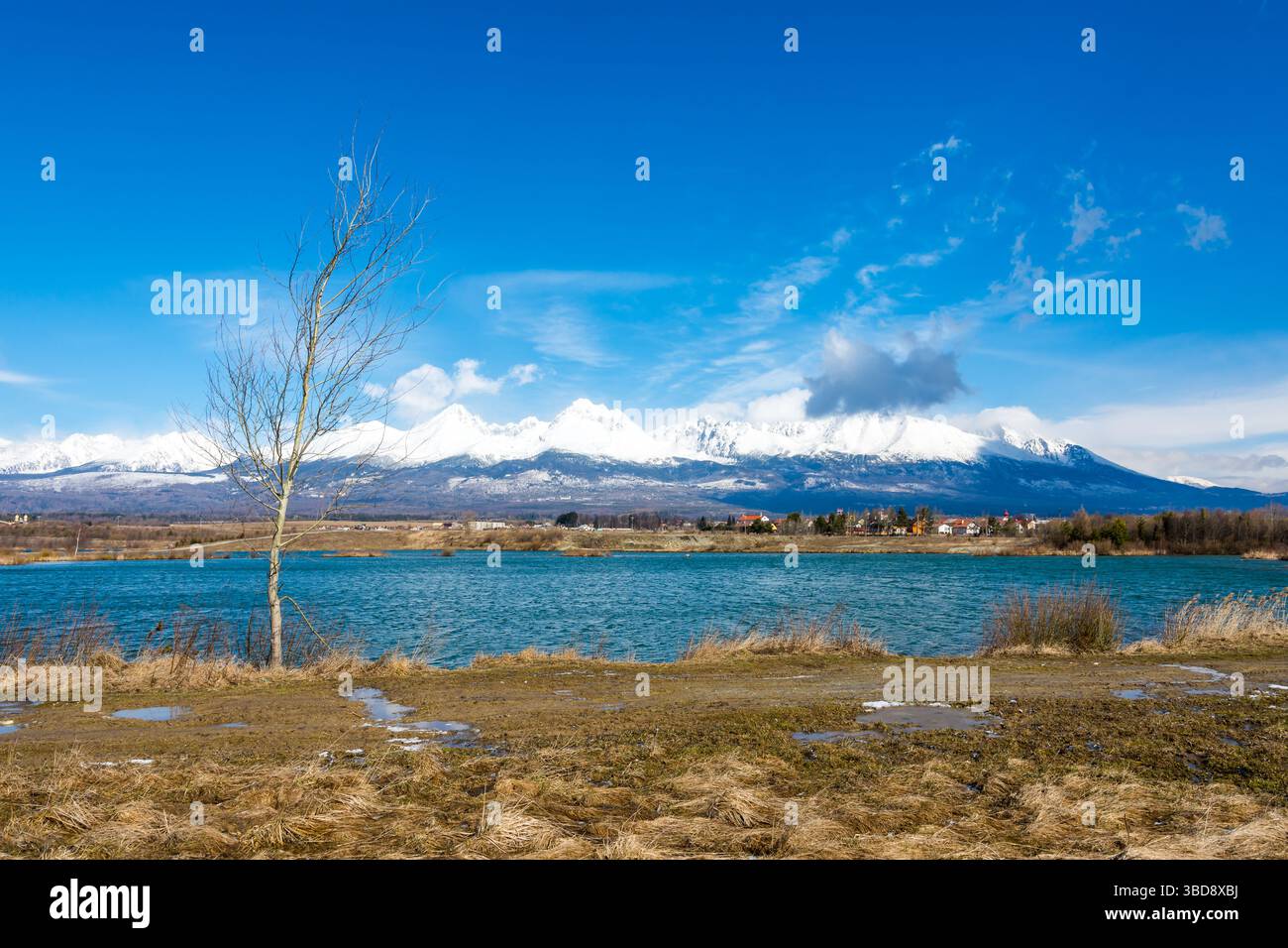 Slovaquie : Big Tatras (Vysoke Tatry) au printemps. Grandes montagnes avec la neige et les nuages. Le lac en premier plan. Petit village près de la montagne et Banque D'Images