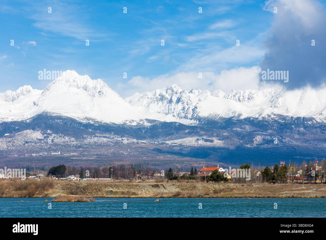 Slovaquie : Big Tatras (Vysoke Tatry) au printemps. Grandes montagnes avec la neige et les nuages. Le lac en premier plan. Petit village près de la montagne et Banque D'Images