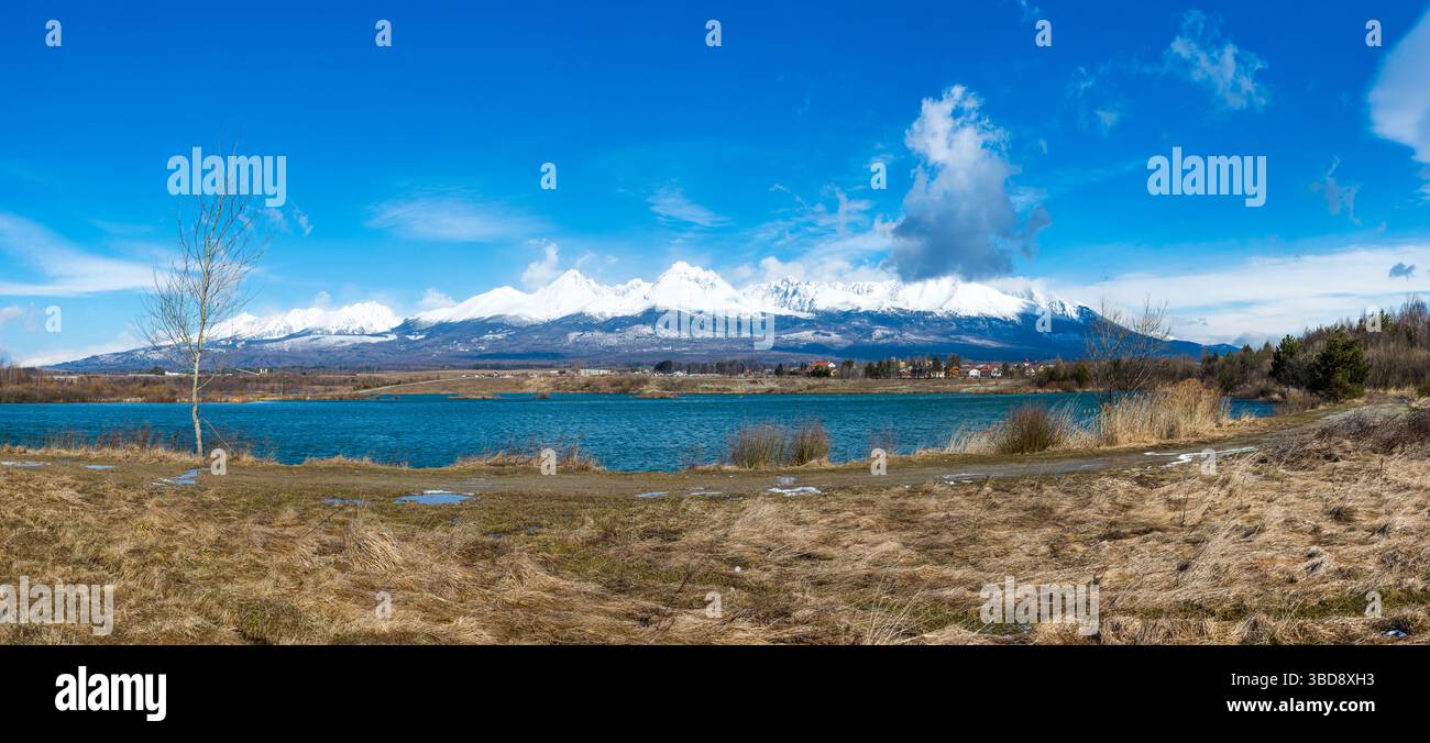 Slovaquie : Big Tatras (Vysoke Tatry) au printemps. Grandes montagnes avec la neige et les nuages. Le lac en premier plan. Petit village près de la montagne et Banque D'Images