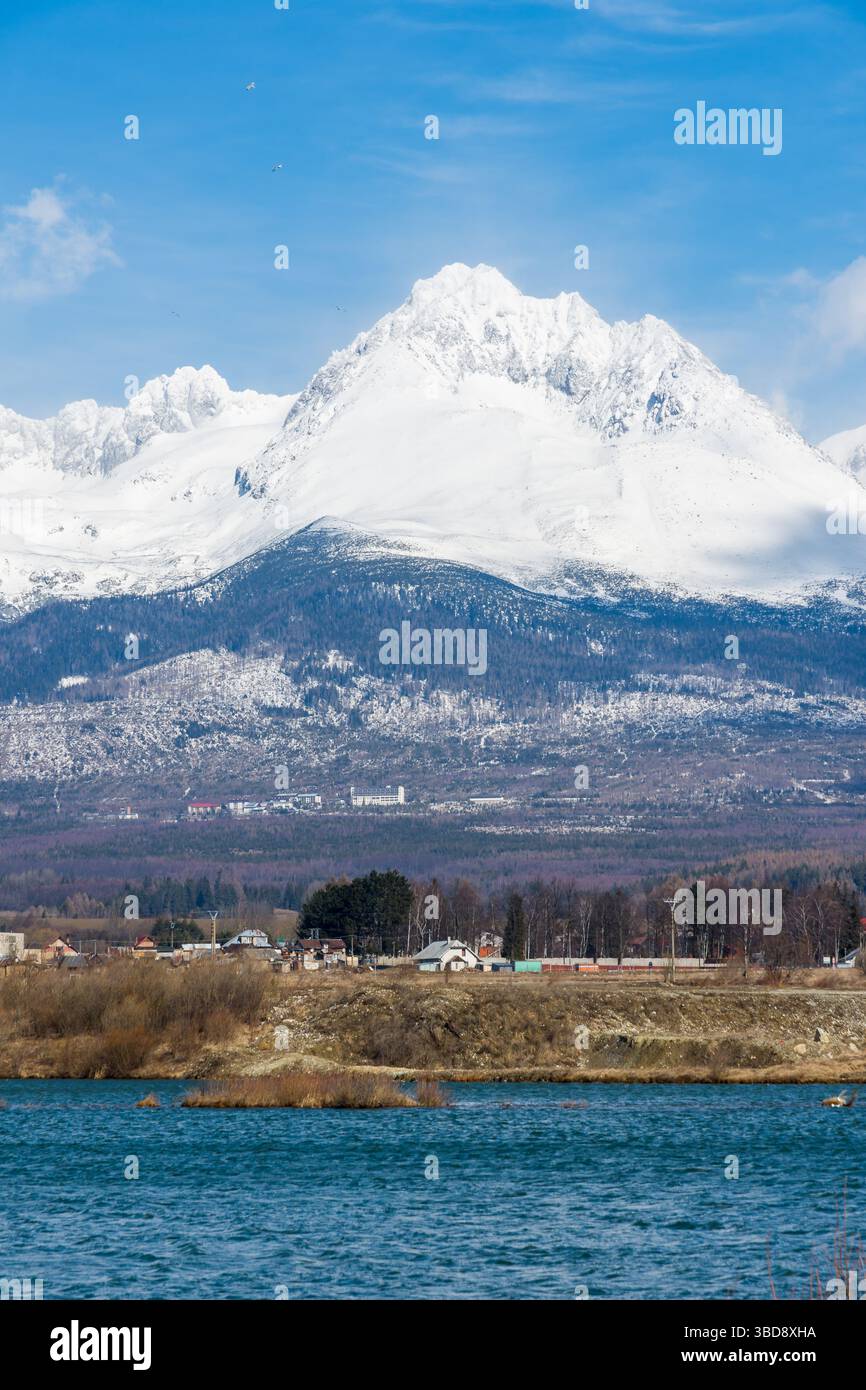 Slovaquie : Big Tatras (Vysoke Tatry) au printemps. Grandes montagnes avec la neige et les nuages. Le lac en premier plan. Petit village près de la montagne et Banque D'Images