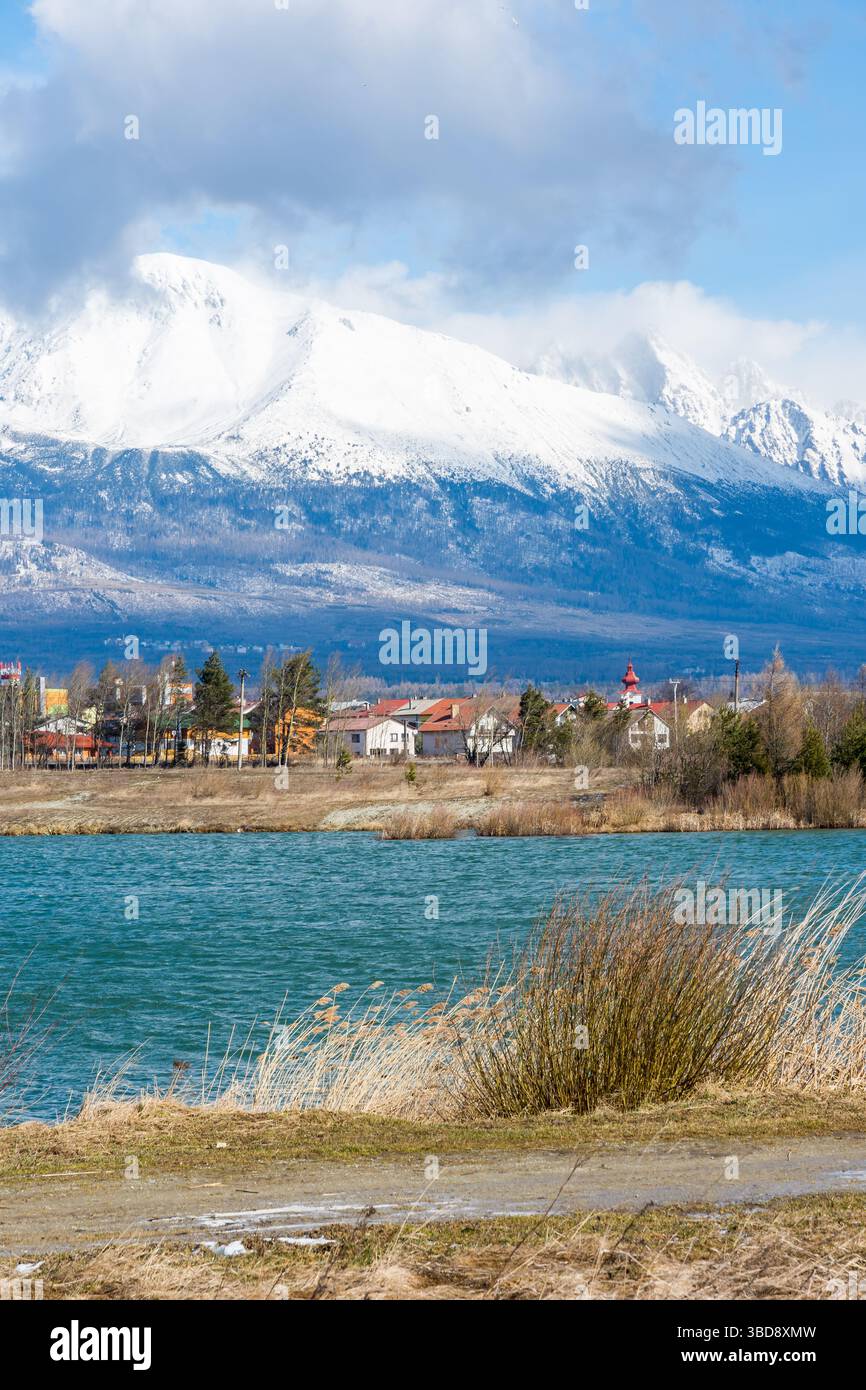 Slovaquie : Big Tatras (Vysoke Tatry) au printemps. Grandes montagnes avec la neige et les nuages. Le lac en premier plan. Petit village près de la montagne et Banque D'Images