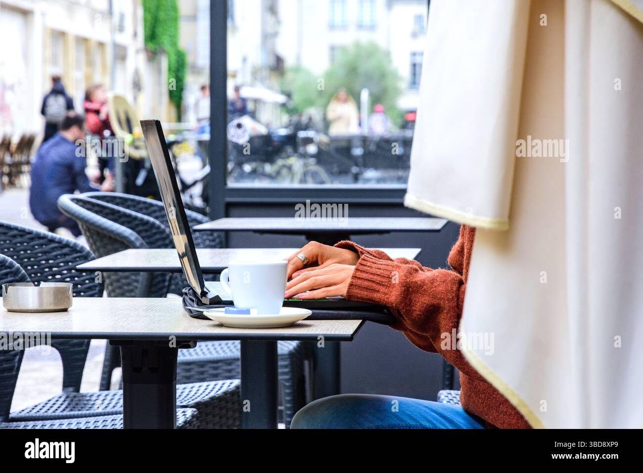 Jeune femme anonyme travaillant sur un ordinateur portable à une table de café en plein air - Tours, Indre-et-Loire (37), France. Banque D'Images