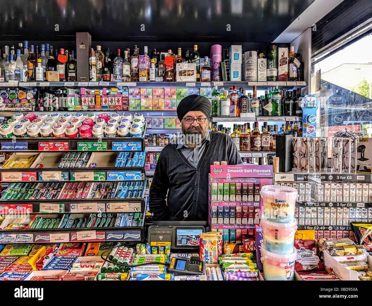 Agent de presse immigrés de première génération d'origine punjabi servant les clients dans son magasin familial du coin, représentant l'entrepreneuriat sud-asiatique Banque D'Images
