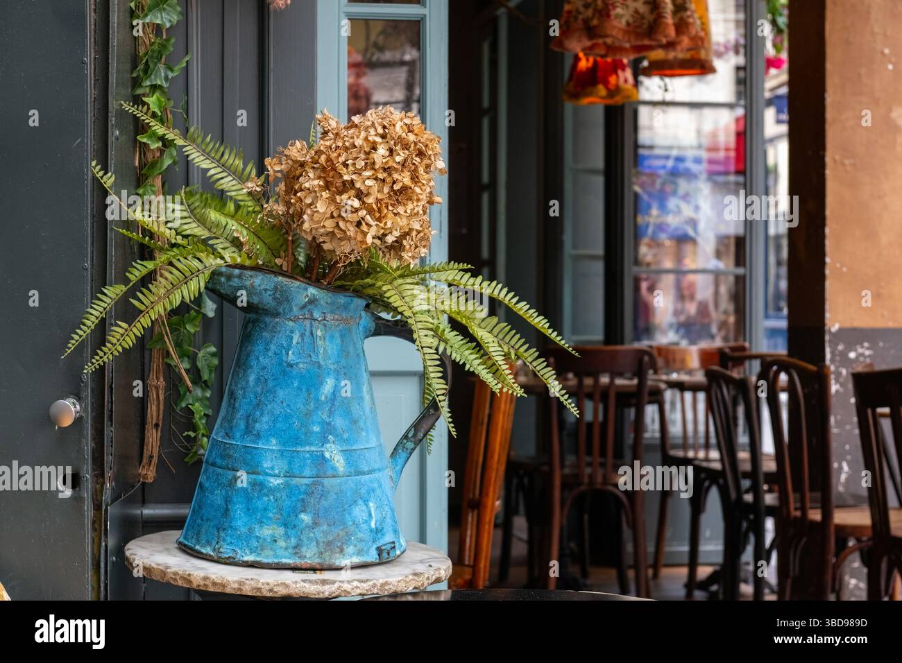 Une cruche en métal bleu utilisée comme vase dans un café. Banque D'Images