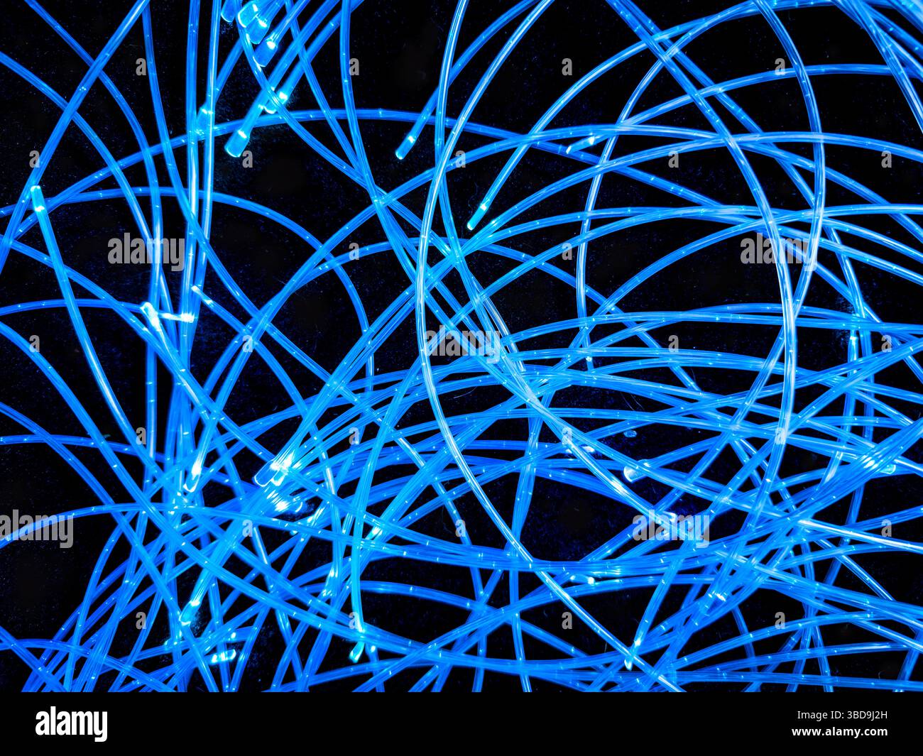 Arrangement abstrait de lumières LED bleues allumées ou allumées sur des fils enroulés sur un fond noir Banque D'Images