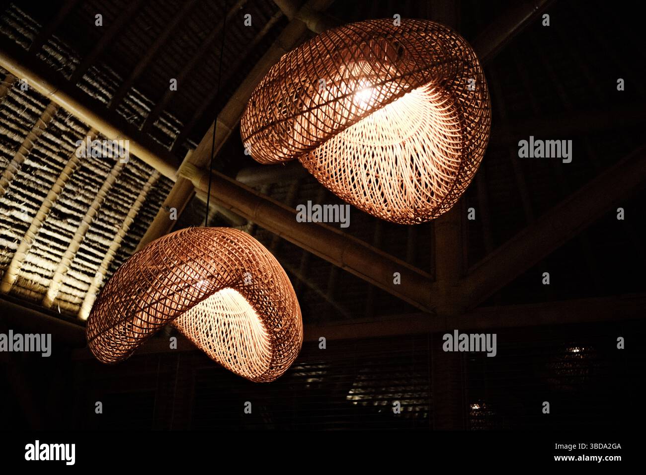 Lueur chaude de lumières suspendues décoratives en rotin tissé dans un intérieur en bambou Banque D'Images