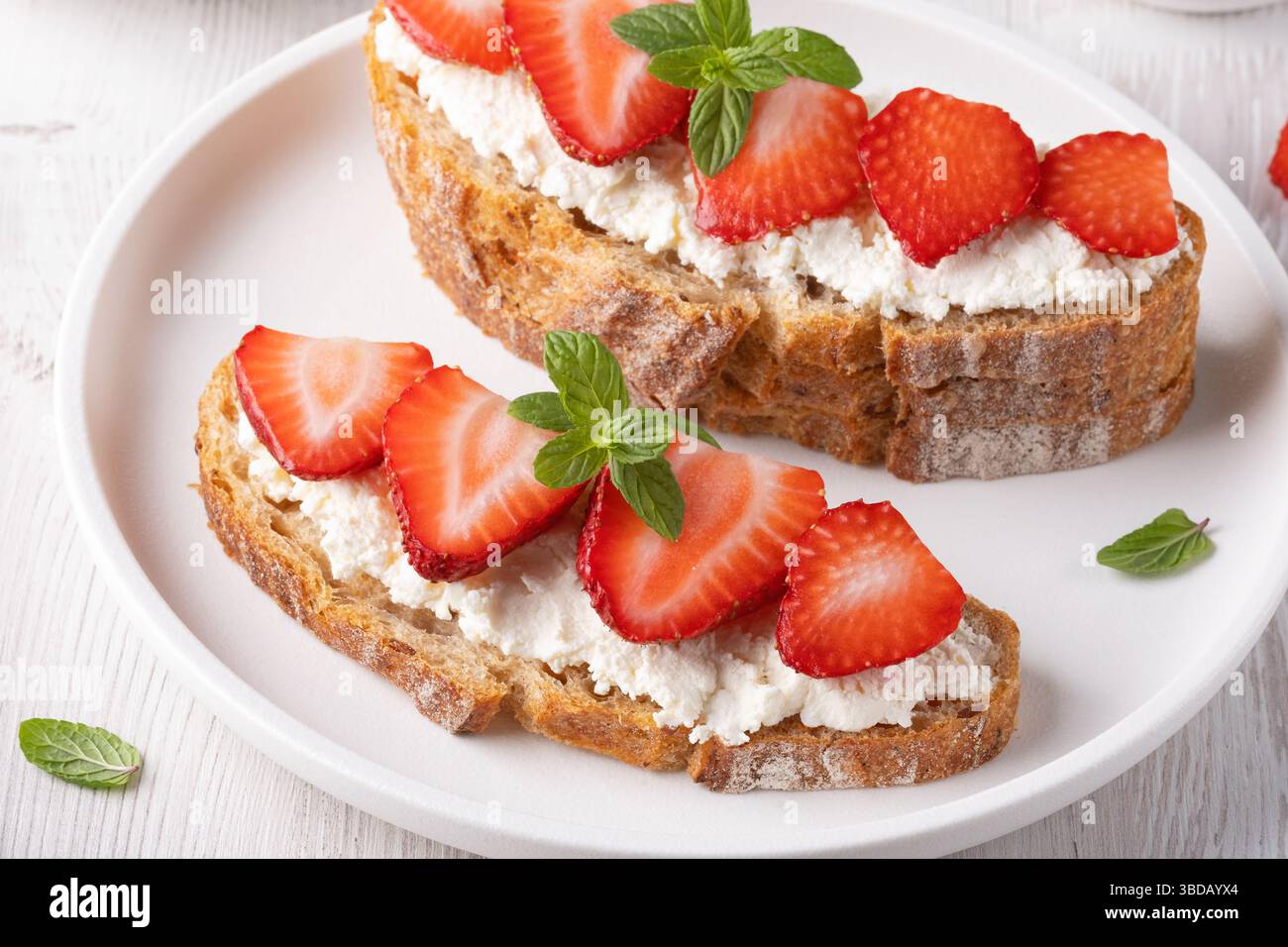 Toast aux fraises fraîchement préparé avec du fromage à pâte molle sur du pain de grains entiers servi sur une assiette blanche Banque D'Images
