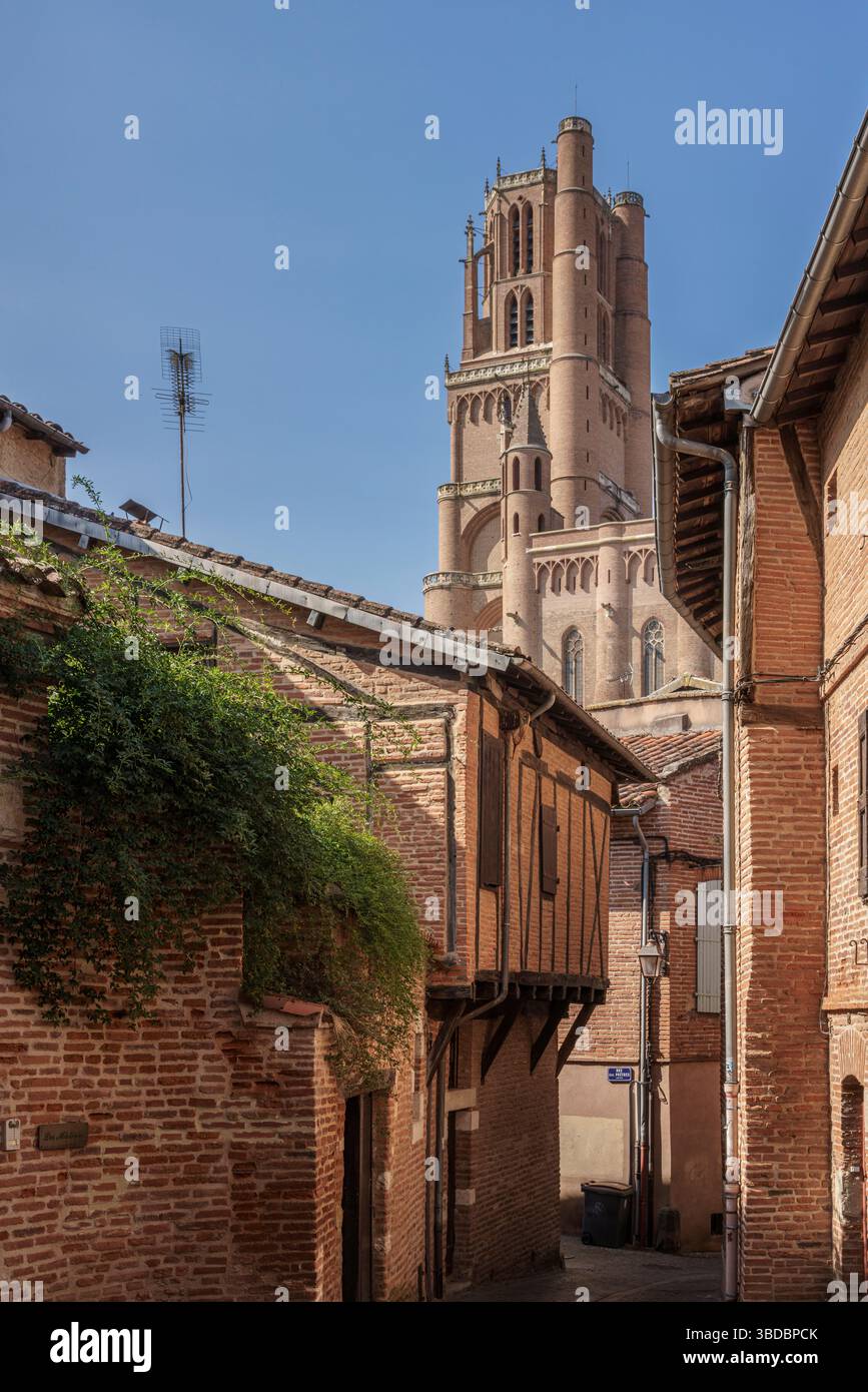 La tour de la cathédrale Sainte Cécile s'élève au-dessus des rues étroites de la vieille ville à Albi France encadrée par une végétation luxuriante et des façades médiévales en briques à proximité. Banque D'Images