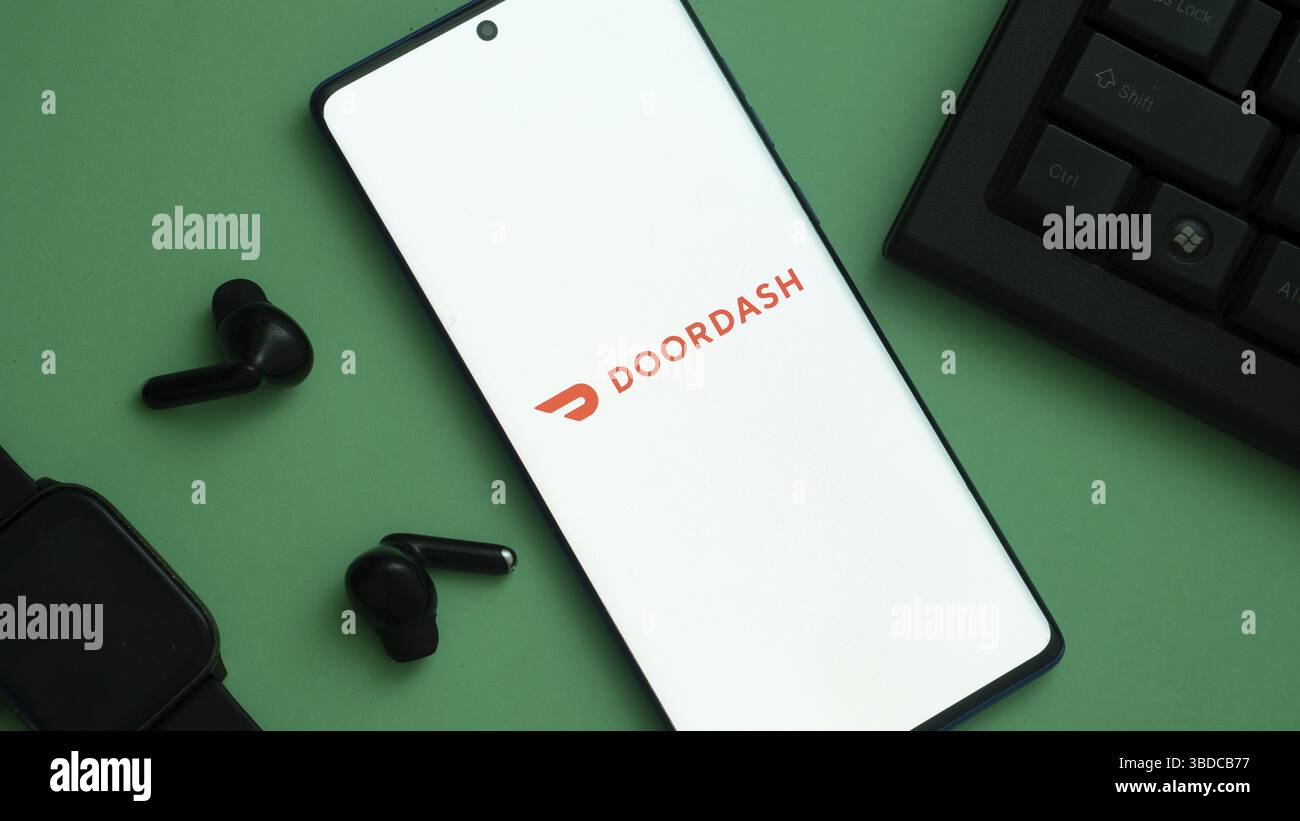 Smartphone avec logo DoorDash à côté des écouteurs et montre sur vert Banque D'Images