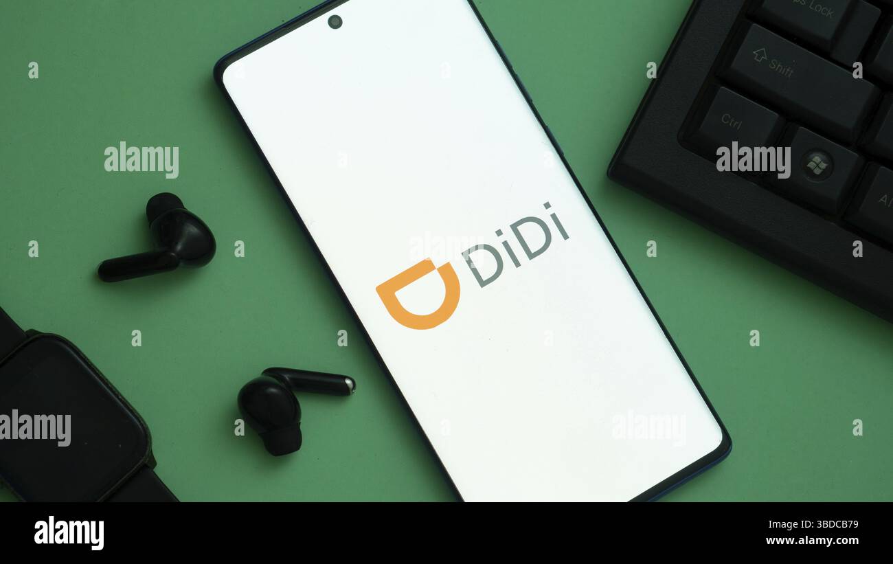 Smartphone avec logo Didi à côté des écouteurs et une montre sur la surface verte Banque D'Images