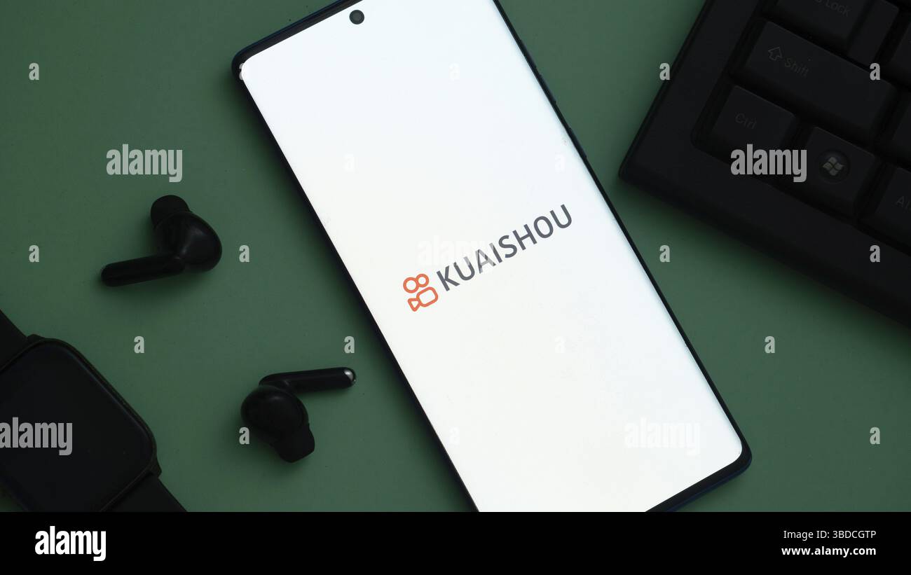 Smartphone affichant le logo Kuaishou, avec écouteurs noirs et smartwatch sur fond vert Banque D'Images