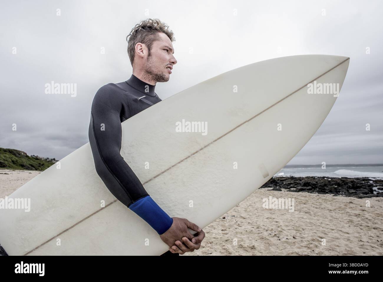 Portrait d'un surfeur debout sur la plage de Super tube à Jeffreys Bay tout en tenant une planche de surf sous son bras Banque D'Images