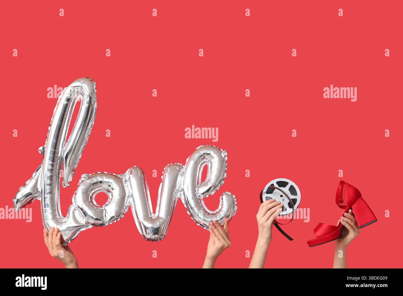 Mains féminines avec ballon d'air en forme de mot AMOUR, chaussure à talon et bobine de film sur fond rouge. Célébration de la Saint-Valentin Banque D'Images