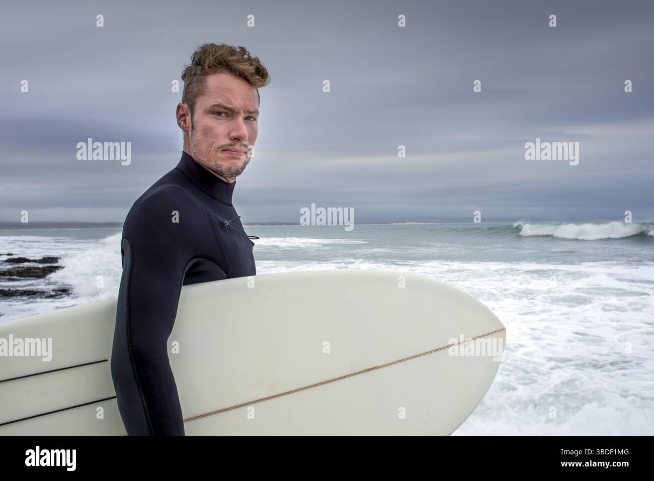 Portrait d'un surfeur avec sa planche de surf sous le bras alors qu'il se tient près de la plage Banque D'Images