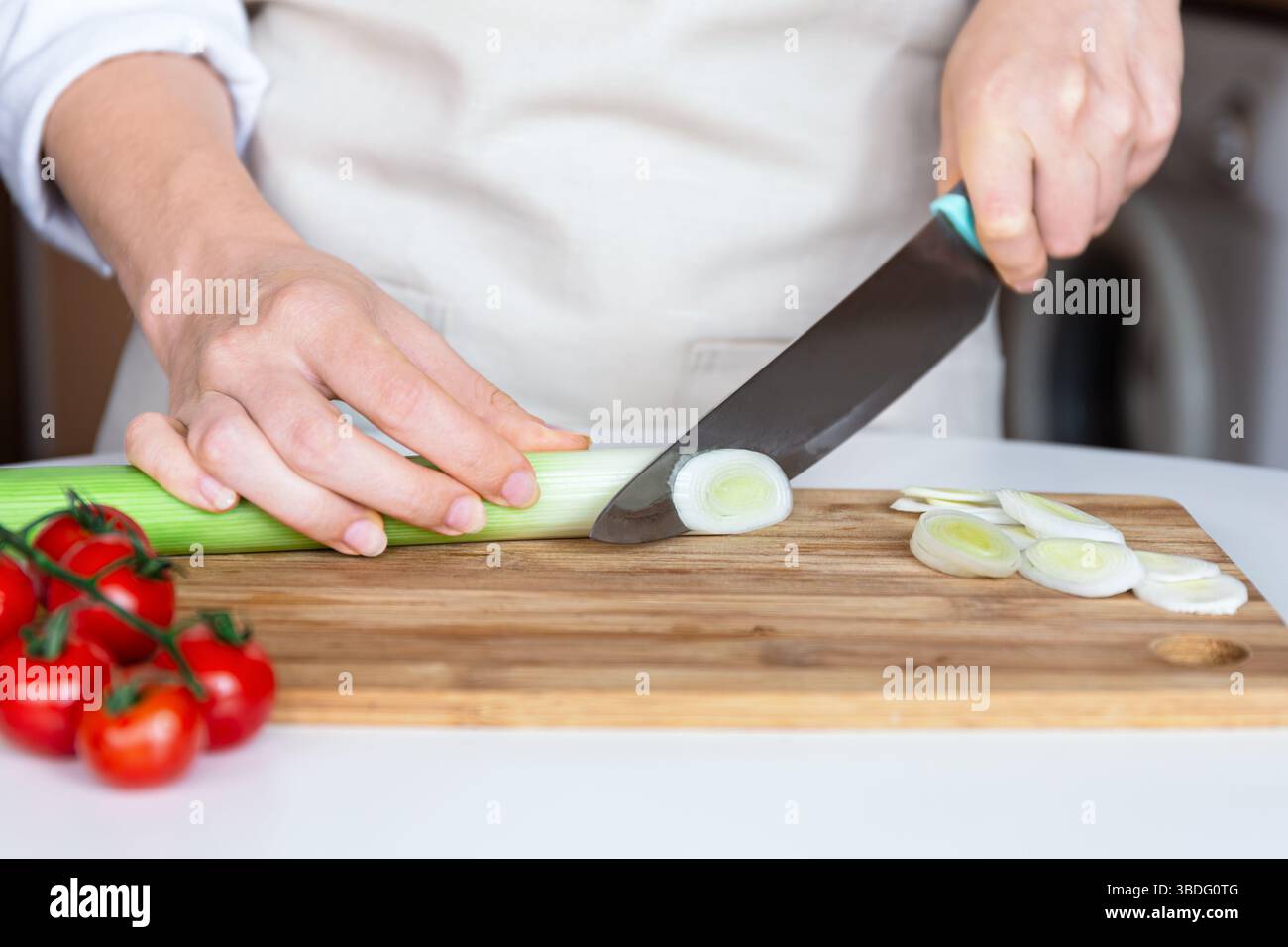Gros plan des mains coupant des poireaux en anneaux sur une planche de bois avec un couteau, préparation des aliments, cuisine saine Banque D'Images