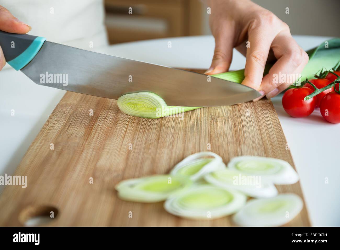 Main avec un couteau tranchant le poireau vert en anneaux sur planche de bois dans la table de cuisine, routine de cuisson, recette de légumes Banque D'Images
