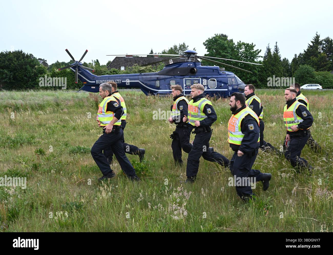 Nordhorn, Allemagne. 24 mai 2025. Les policiers fédéraux se rendent à pied à un poste de contrôle temporaire sur la route fédérale B213 après avoir été déposés par un hélicoptère de police (l). L'opération prioritaire a lieu dans le cadre du rétablissement temporaire des contrôles aux frontières intérieures le long de la frontière entre la basse-Saxe et les pays-Bas. Crédit : Lars Penning/dpa/Alamy Live News Banque D'Images