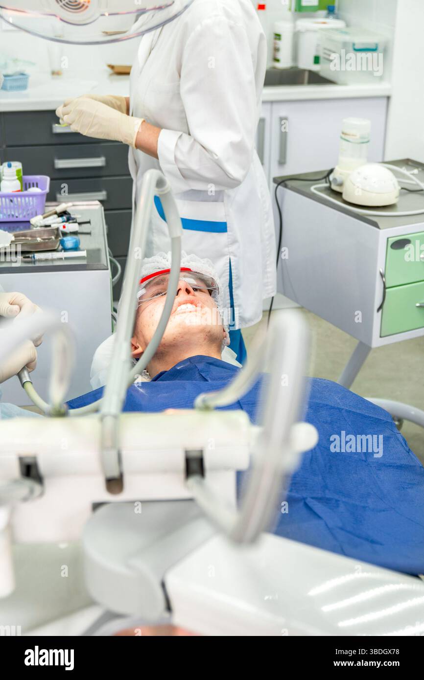 Adolescent montre de l'insatisfaction en étant allongé dans une chaise dentaire, se préparant à des traitements dentaires dans une clinique Banque D'Images