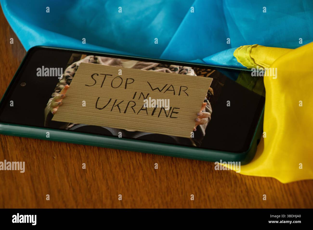 Affiche avec le texte Stop War in Ukraine dans les mains d'une fille sur l'écran d'un smartphone allongé sur une table avec un drapeau ukrainien, message anti-guerre Banque D'Images