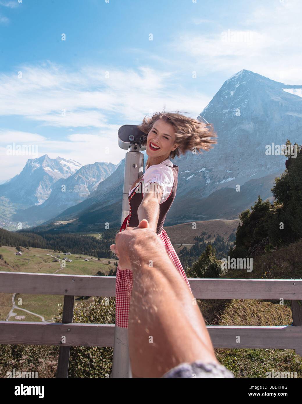 Belle femme portant des vêtements traditionnels bavarois - dirndl ou tracht regarde le paysage des Alpes européennes à travers des jumelles en Suisse Banque D'Images