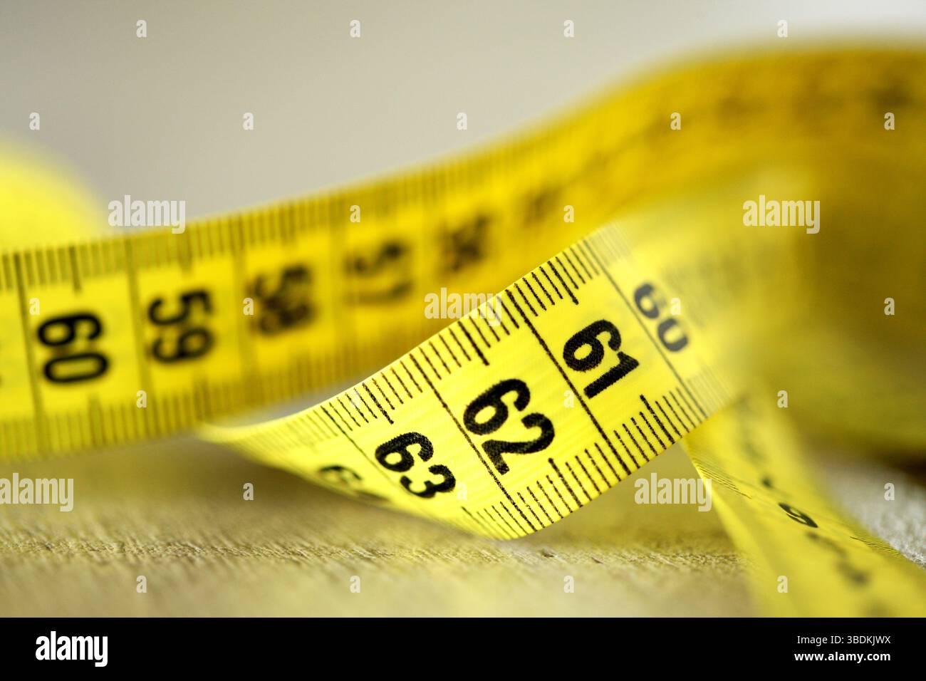 Gros plan d'un ruban à mesurer jaune sur fond blanc, avec réflexion sous. Taille de taille irréaliste, symbolisant la forme physique, exigence de modèle. Banque D'Images