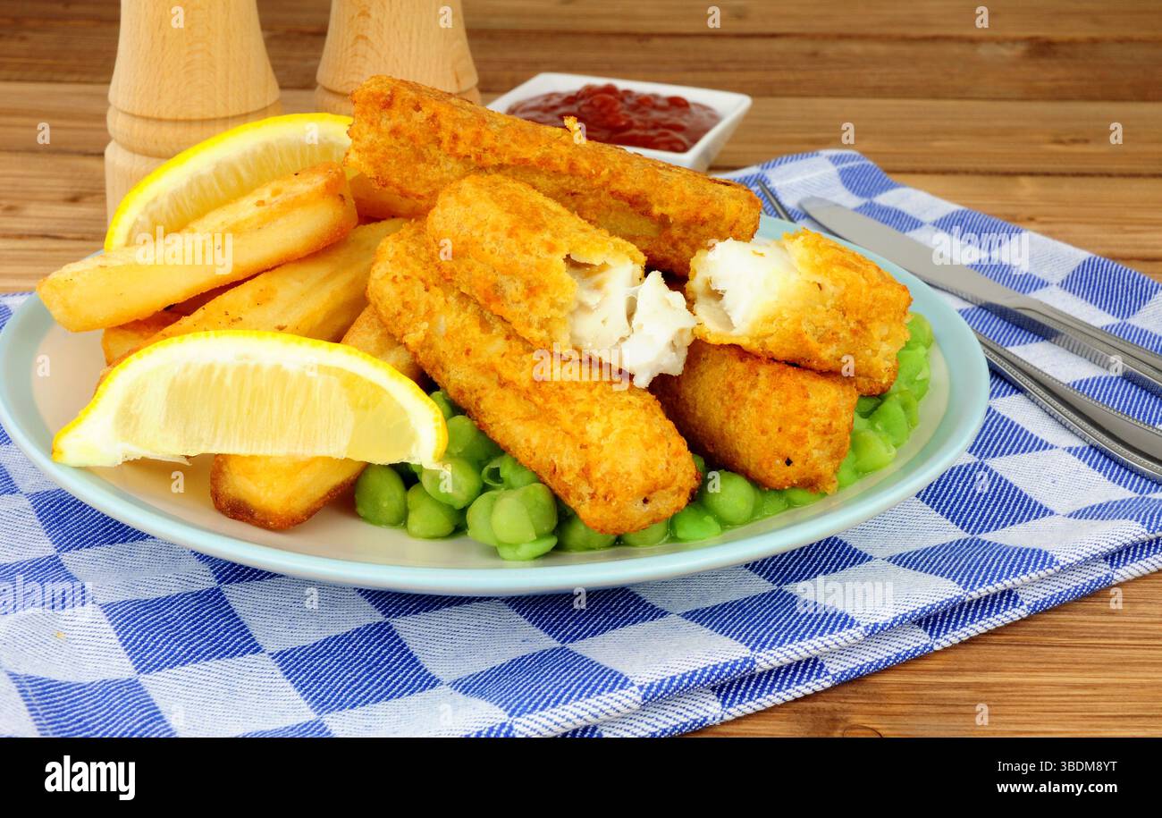 Les doigts de poisson et les chips couverts de pâte à frire sont repas avec des petits pois sur fond de bois Banque D'Images