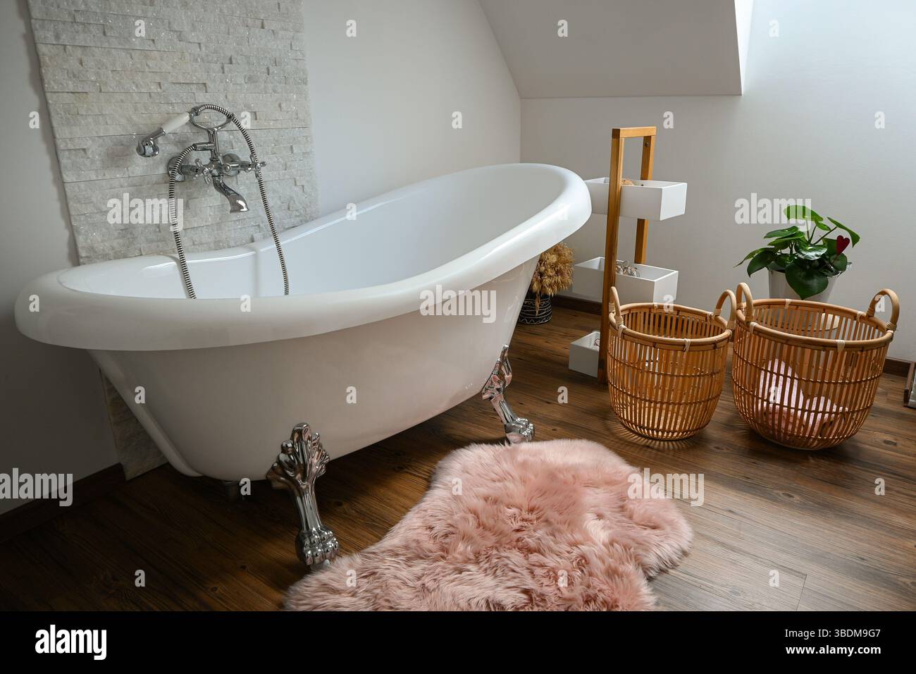 Salle de bains luxueuse dotée d'une baignoire îlot, d'un tapis rose, de paniers en osier et d'une touche d'élégance. Banque D'Images